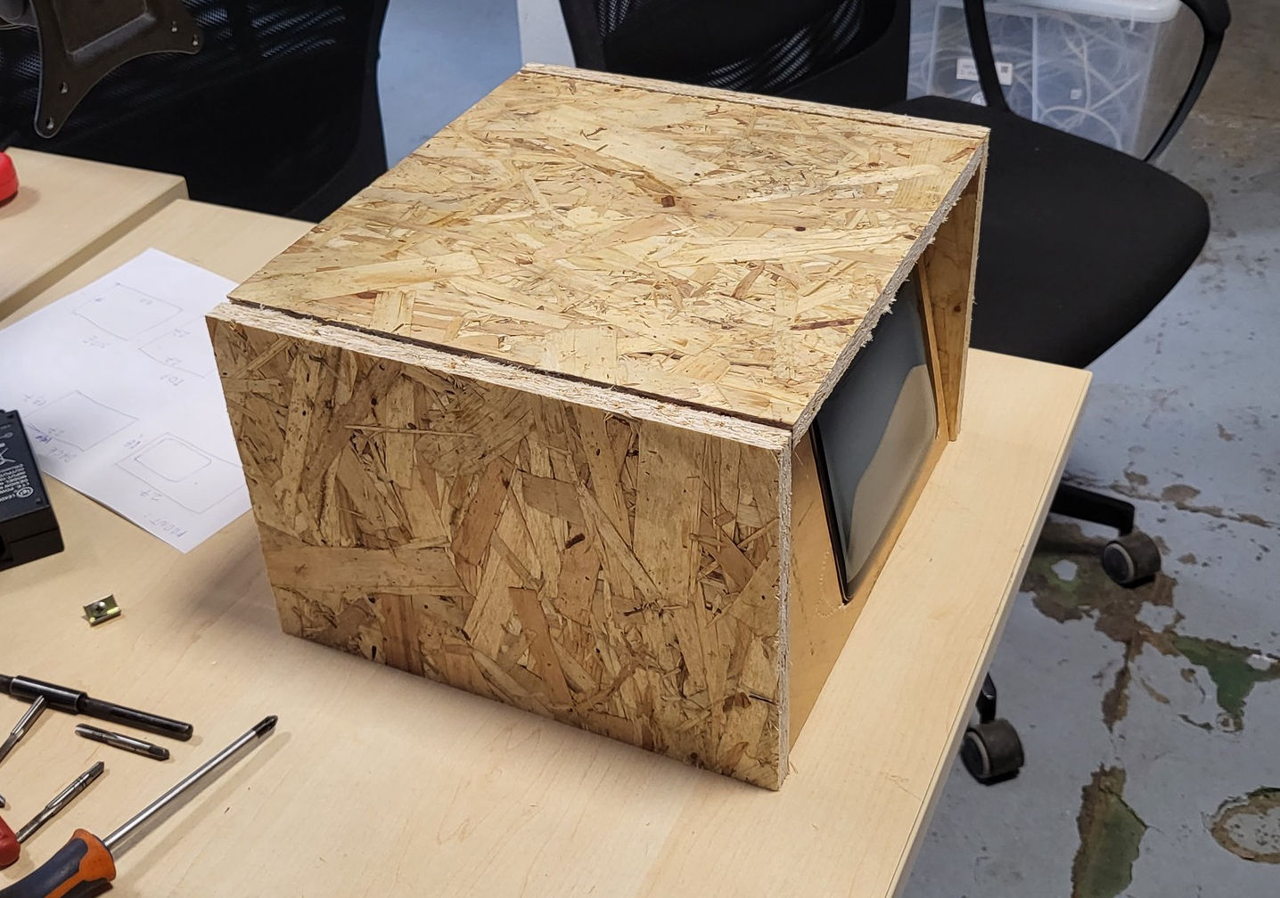 A big, square-ish box is sitting on a table; on one side, it has an indent and a cutout for a CRT.