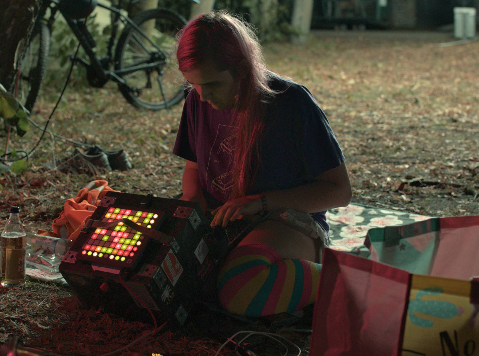 picture of me in a forest-y area on cccamp23; i'm doing something on the luggable, which rests partially on the ground. the luggable has a bunch of blinky lights on top of it